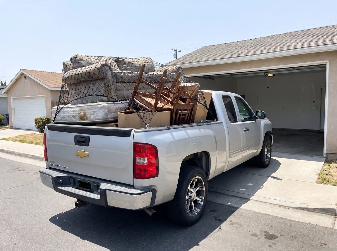 Truck bed heaped with old furniture secured under a cargo net for a dump run